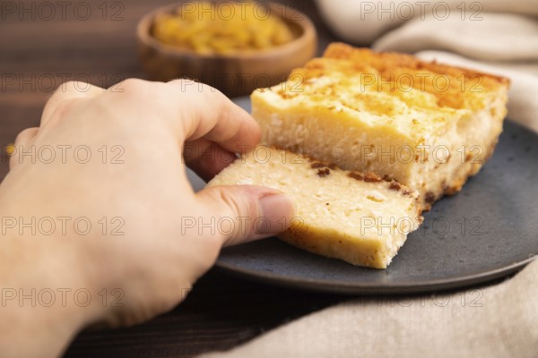 ?ottage cheese ?asserole, Curd cake, with dried apricots and raisins with hand on brown wooden background and linen textile, side view, close up, minimalism, selective focus