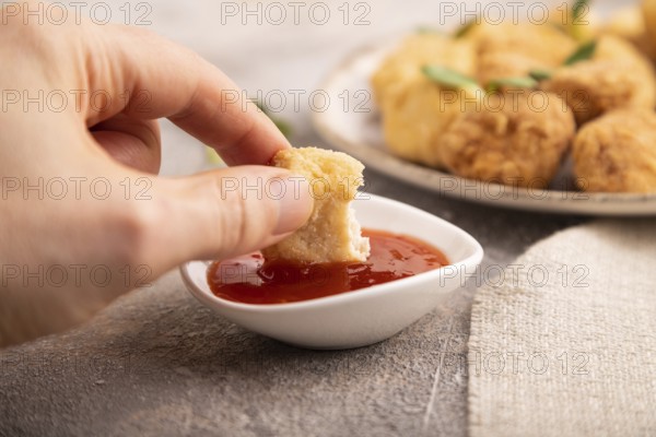 Fried crispy Chicken Nuggets with ketchup, microgreen on brown concrete background and linen textile with hand. side view, close up, selective focus