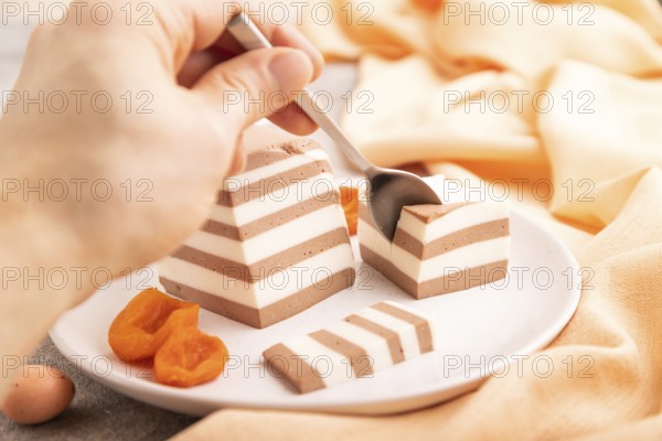 Cocoa and milk jelly with dried apricots with hand on brown concrete background and orange textile, side view, close up, selective focus, minimalism