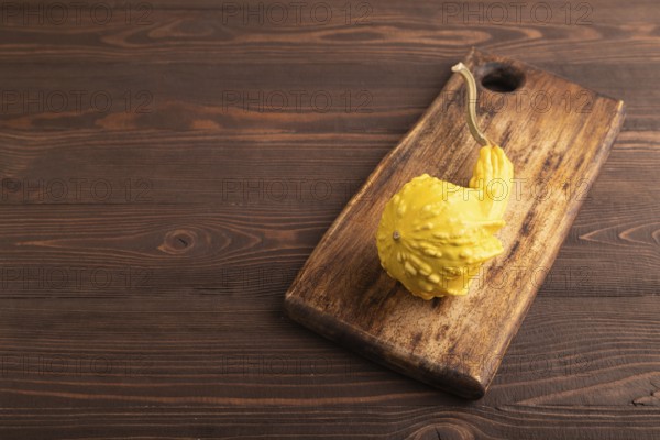 Decorative orange Pumpkin on cutting board on brown wooden background, side view, copy space, minimalism