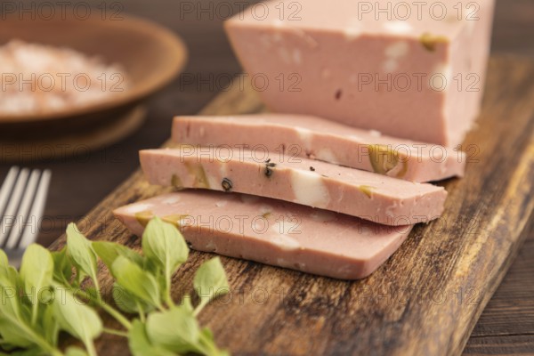 Mortadella sausage on wooden cutting board with pepper and herbs on brown wooden background. Side view, close up, selective focus