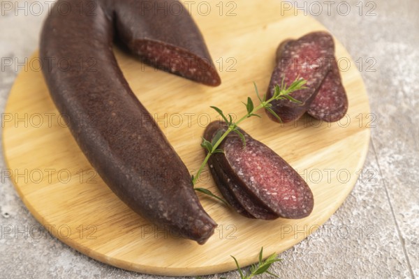 Sujuk sausage on wooden cutting board with pepper and herbs on brown concrete background. Side view, close up, selective focus