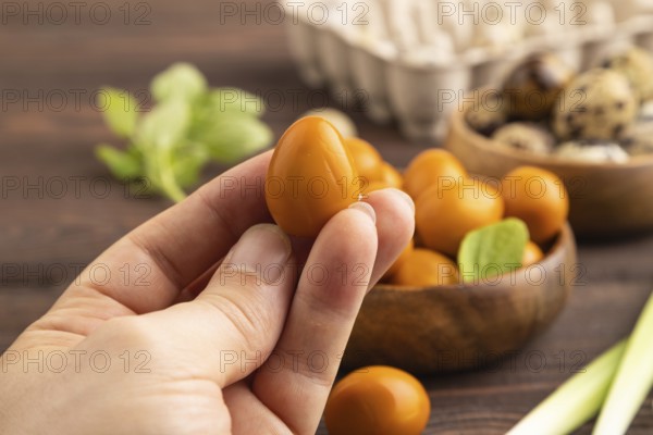 Pile of Smoked Quail eggs in bowl with hand on a brown wooden background. side view, close up, selective focus