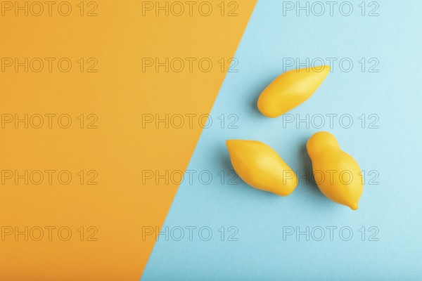 Yellow tomatoes on blue and orange pastel paper background. Top view, copy space, flat lay. healthy food, vegetable, minimalism