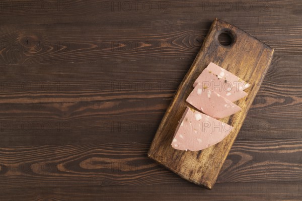 Mortadella sausage on wooden cutting board with pepper and herbs on brown wooden background. Top view, flat lay, copy space