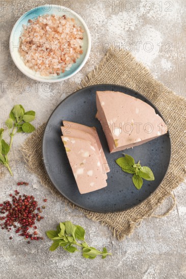Mortadella sausage on plate with pepper and herbs on brown concrete background and linen textile. Top view, flat lay, close up