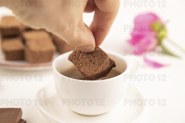 Chocolate marshmallow with cup of coffee with hand on white wooden background. side view, close up, selective focus