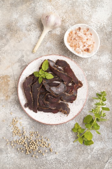 Armenian Basturma dried meat on plate with pepper and herbs on brown concrete background. Top view, flat lay, copy space