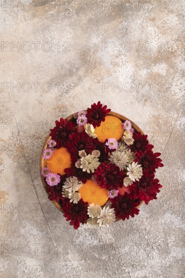 Wooden bowl with carrot slices and red Chrysanthemum flowers, Astrantia flowers, flower salad on brown concrete background, top view, flat lay, copy space, minimalism