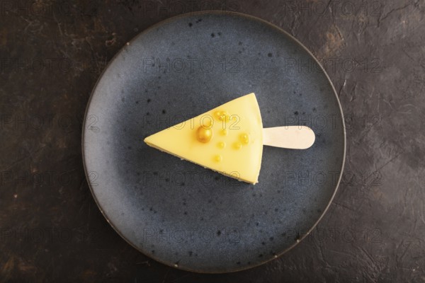 Yellow Cake pop with sprinkles on blue ceramic plate on black concrete background, top view, flat lay, close up, minimalism