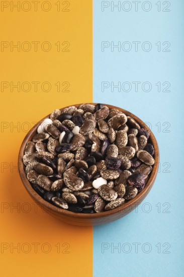 Wooden bowl with Kidney beans on blue and orange pastel paper background, side view, copy space, minimalism