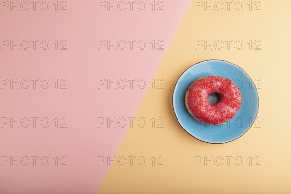 Pink Donut with sprinkles on blue ceramic plate on blue and orange pastel paper background, top view, flat lay, copy space, minimalism