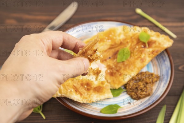 Fried homemade Khachapuri cake with cheese and meat, fried in pan with hand. Traditional Georgian cuisine on brown wooden background. Side view, close up, selective focus