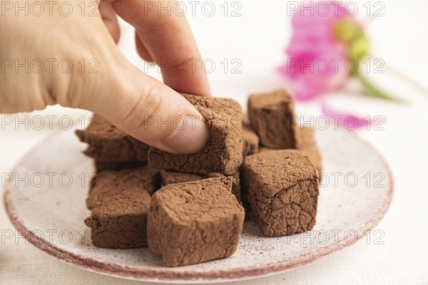 Chocolate marshmallow with cup of coffee with hand on white wooden background. side view, close up, selective focus