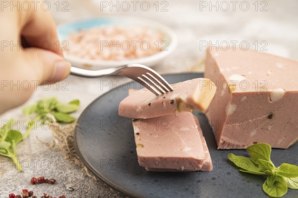 Mortadella sausage with hand on plate with pepper and herbs on brown concrete background and linen textile. Side view, close up, selective focus