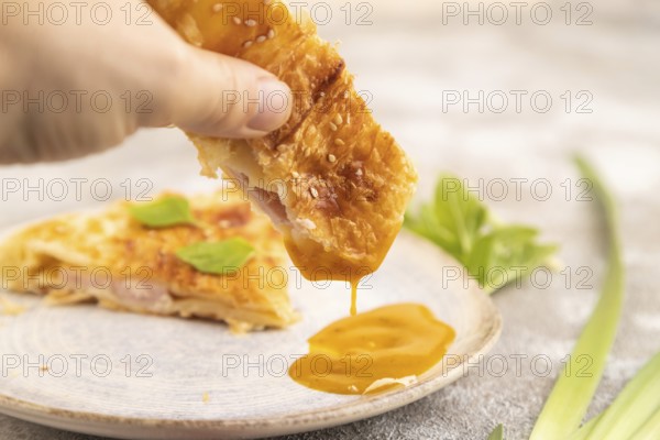 Fried homemade Khachapuri cake with hand with cheese and meat, fried in pan. Traditional Georgian cuisine on brown concrete background. Side view, close up, selective focus