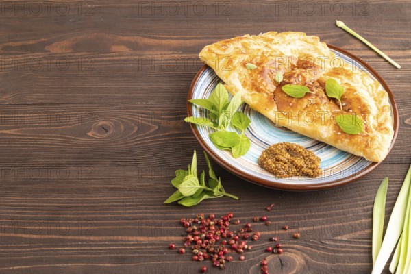 Fried homemade Khachapuri cake with cheese and meat, fried in pan. Traditional Georgian cuisine on brown wooden background. Side view, copy space