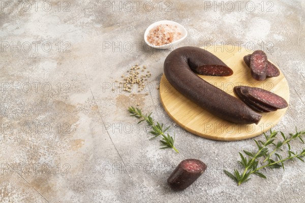 Sujuk sausage on wooden cutting board with pepper and herbs on brown concrete background. Side view, copy space