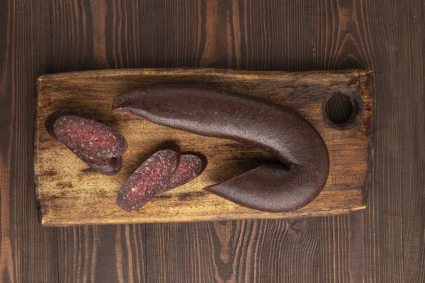 Sujuk sausage on wooden cutting board with pepper and herbs on brown wooden background. Top view, flat lay, copy space