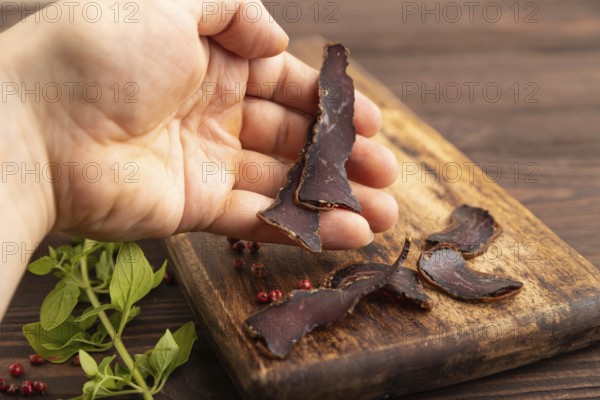 Armenian Basturma dried meat with hand on wooden cutting board with pepper and herbs on brown wooden background. Side view, close up, selective focus