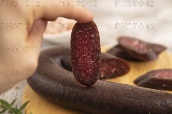 Sujuk sausage with hand on wooden cutting board with pepper and herbs on brown concrete background. Side view, close up, selective focus