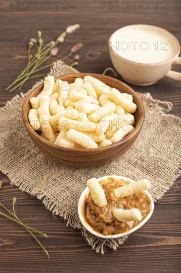 Corn flakes sticks with caramel in wooden bowl on brown wooden background and linen textile. Side view, close up