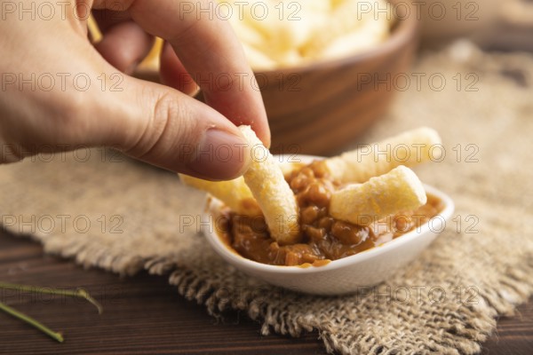 Corn flakes sticks with caramel in wooden bowl with hand on brown wooden background and linen textile. Side view, close up, selective focus