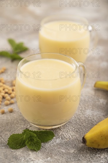 Organic non dairy banana and soy milk in glass on brown concrete background. Vegan healthy food concept, side view, close up, selective focus