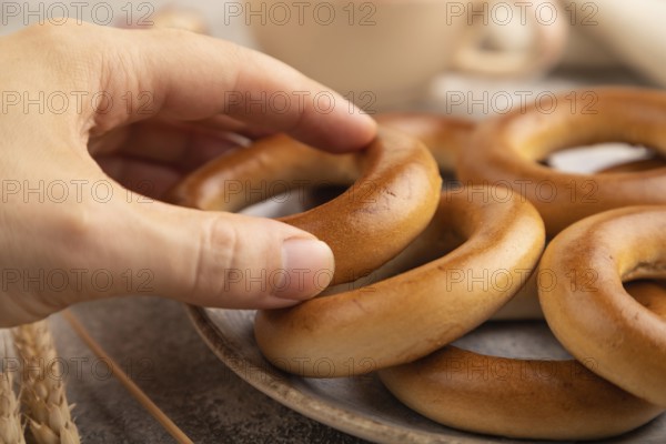 Homemade Ring Bagel with hand with cup of coffee on brown concrete background and linen textile. side view, close up, selective focus