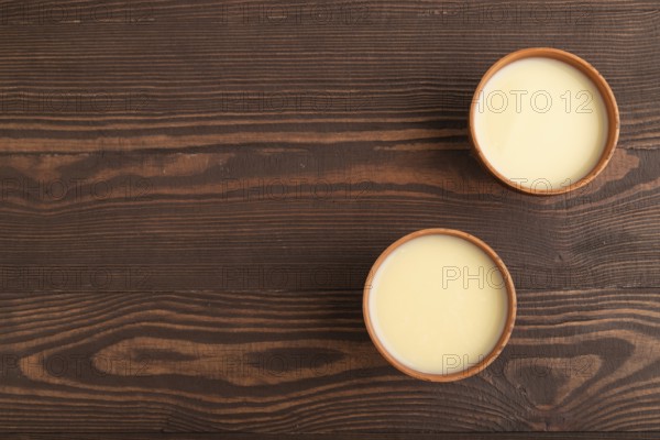 Organic non dairy banana and soy milk in clay cup on brown wooden background. Vegan healthy food concept, flat lay, top view, copy space