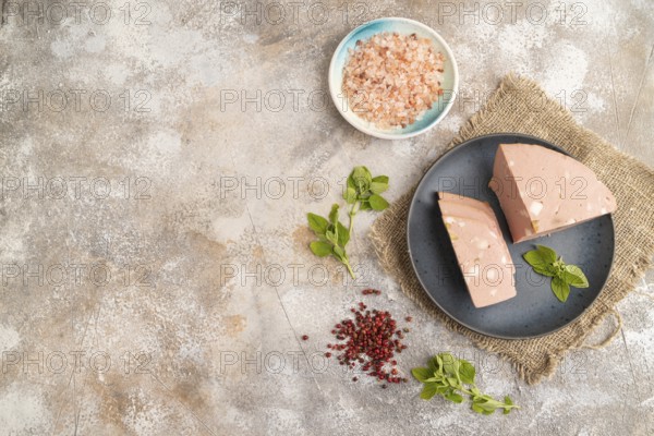 Mortadella sausage on plate with pepper and herbs on brown concrete background and linen textile. Top view, flat lay, copy space