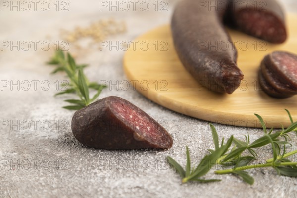 Sujuk sausage on wooden cutting board with pepper and herbs on brown concrete background. Side view, close up, selective focus