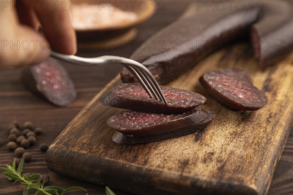 Sujuk sausage with hand on wooden cutting board with pepper and herbs on brown wooden background. Side view, close up, selective focus