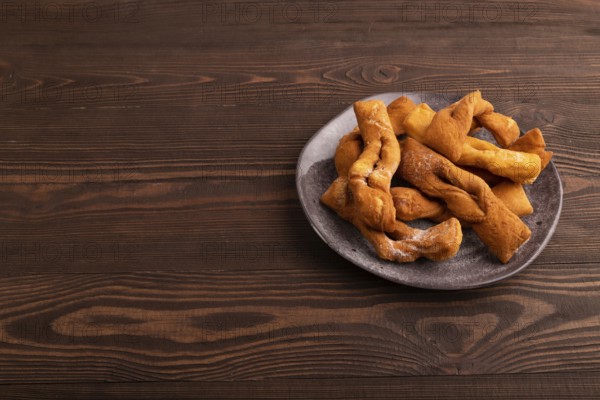 Crunchy biscuit Brushwood cookies sprinkled with powdered sugar on brown wooden background, side view, copy space