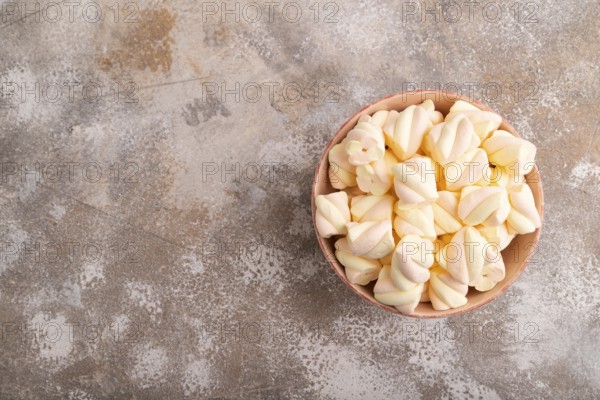 Orange and pink marshmallow in ceramic bowl on brown concrete background, top view, flat lay, copy space, minimalism