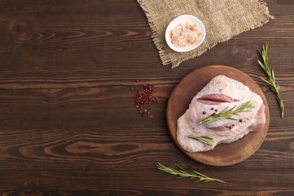 Raw Turkey Thigh with spices and rosemary on cutting board on brown wooden background and linen textile. top view, flat lay, copy space