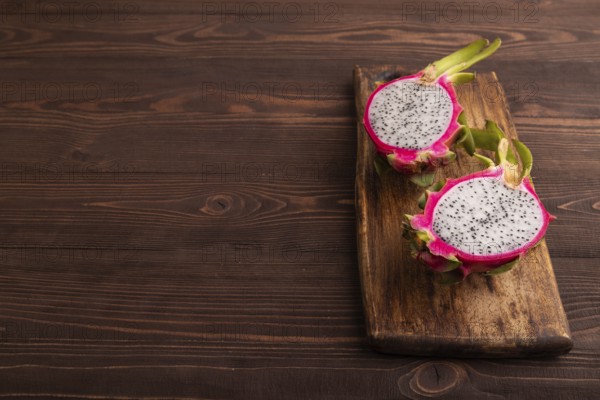 Ripe Pitaya on cutting board on brown wooden background, side view, copy space, minimalism