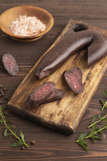Sujuk sausage on wooden cutting board with pepper and herbs on brown wooden background. Side view, close up
