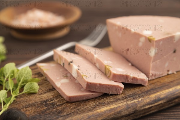 Mortadella sausage on wooden cutting board with pepper and herbs on brown wooden background. Side view, close up, selective focus