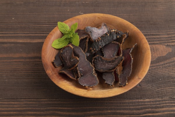 Armenian Basturma dried meat on wooden bowl with pepper and herbs on brown wooden background. Side view, copy space