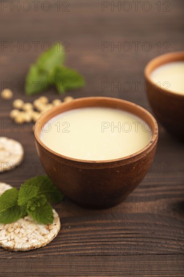 Organic non dairy banana and soy milk in clay cup on brown wooden background. Vegan healthy food concept, side view, close up, selective focus