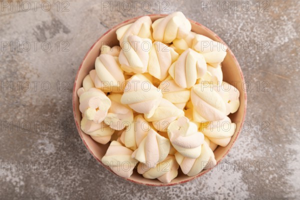 Orange and pink marshmallow in ceramic bowl on brown concrete background, top view, flat lay, copy space, minimalism