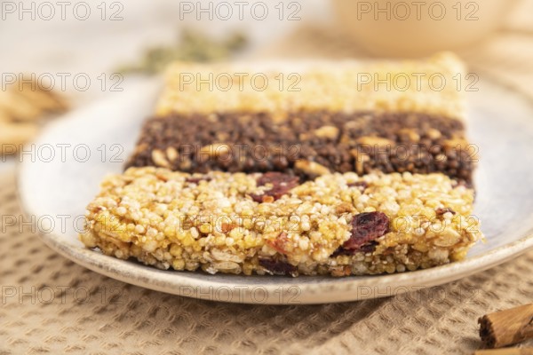 Granola bars with caramel, nuts, flakes in ceramic plate on brown concrete background, beige linen napkin, cup of green tea. Side view, close up, selective focus