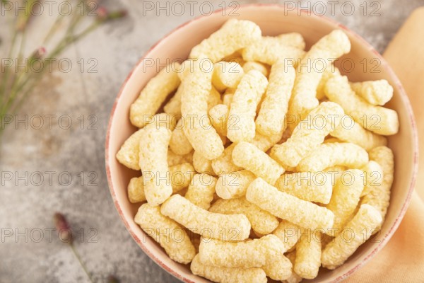 Corn flakes sticks with caramel in ceramic bowl on gray concrete background and orange linen textile. Top view, flat lay, close up
