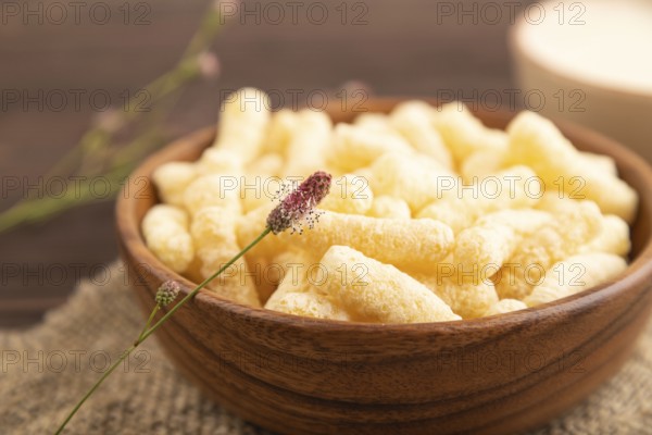 Corn flakes sticks with caramel in wooden bowl on brown wooden background and linen textile. Side view, close up, selective focus