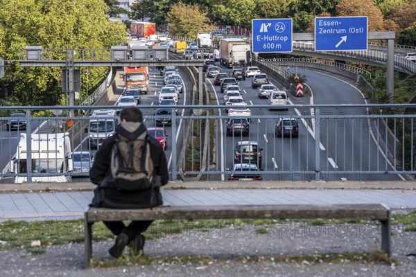 Man sitting on a bench, looking at the traffic jam on the A40 motorway, Ruhrschnellweg, in the city passage of Essen, at Europaplatz, entrance to the Ruhrschnellweg tunnel, North Rhine-Westphalia, Germany
