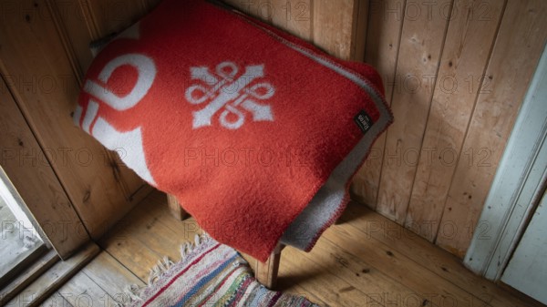 Rote Wolldecke mit Olavsweg-Symbol liegt auf einem Holzschemel, historischer Bauernhof und Pilgerunterkunft Budsjord, Dovre, Pilgerweg Olavsweg oder Olavsleden, Gudbrandsdalen oder Gudbrandstal, Norwegen