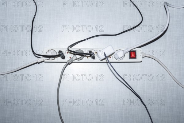 Top view of a power strip with on/off switch and various plugged-in plugs and cables on a white Resopal panel