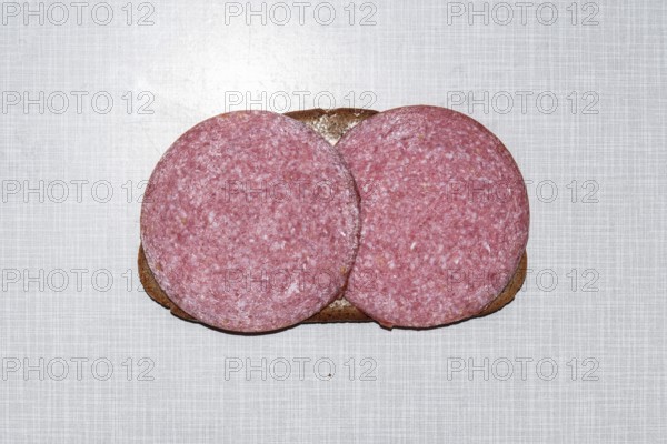 Top shot of a slice of bread smeared with margarine and topped with salami on a white Resopal plate