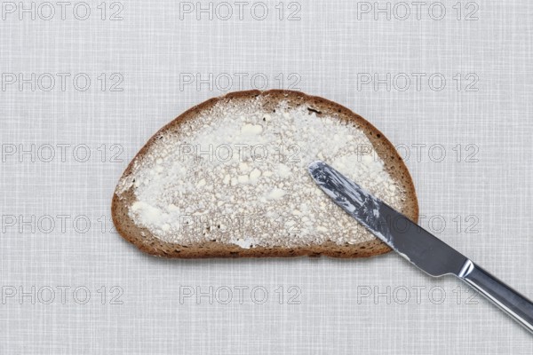 Top shot of a slice of bread smeared with margarine and a knife on a white Resopal plate